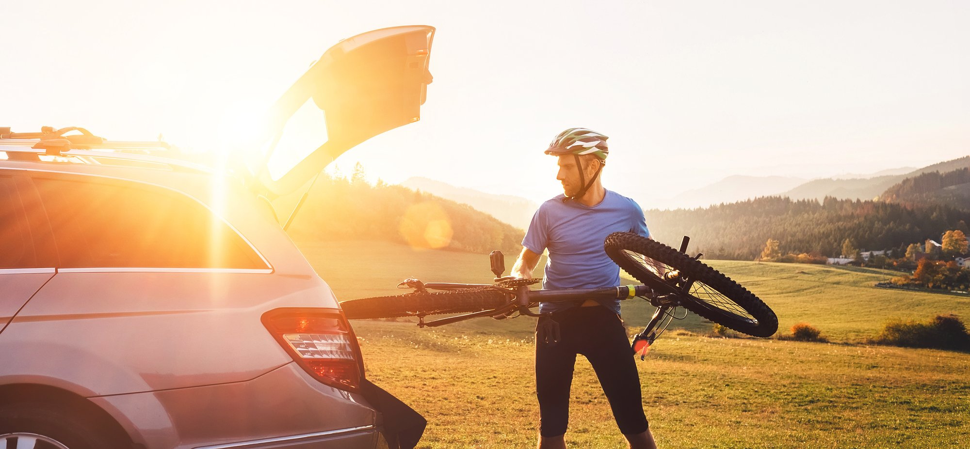 A cyclist loads his bicycle into the trunk of his car, which has been opened with voice activation technology for hands-free operation